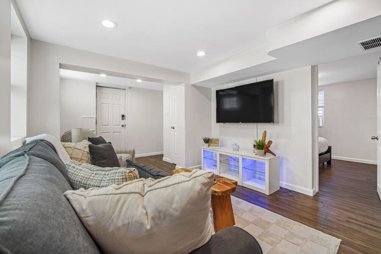 A modern living room with a large sofa, a flat-screen TV mounted on the wall, and a wooden coffee table.