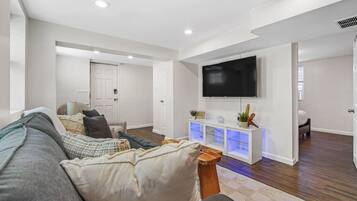 A modern living room with a large sofa, a flat-screen TV mounted on the wall, and a wooden coffee table.