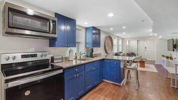 A modern kitchen with blue cabinets, stainless steel appliances, and a wooden floor.