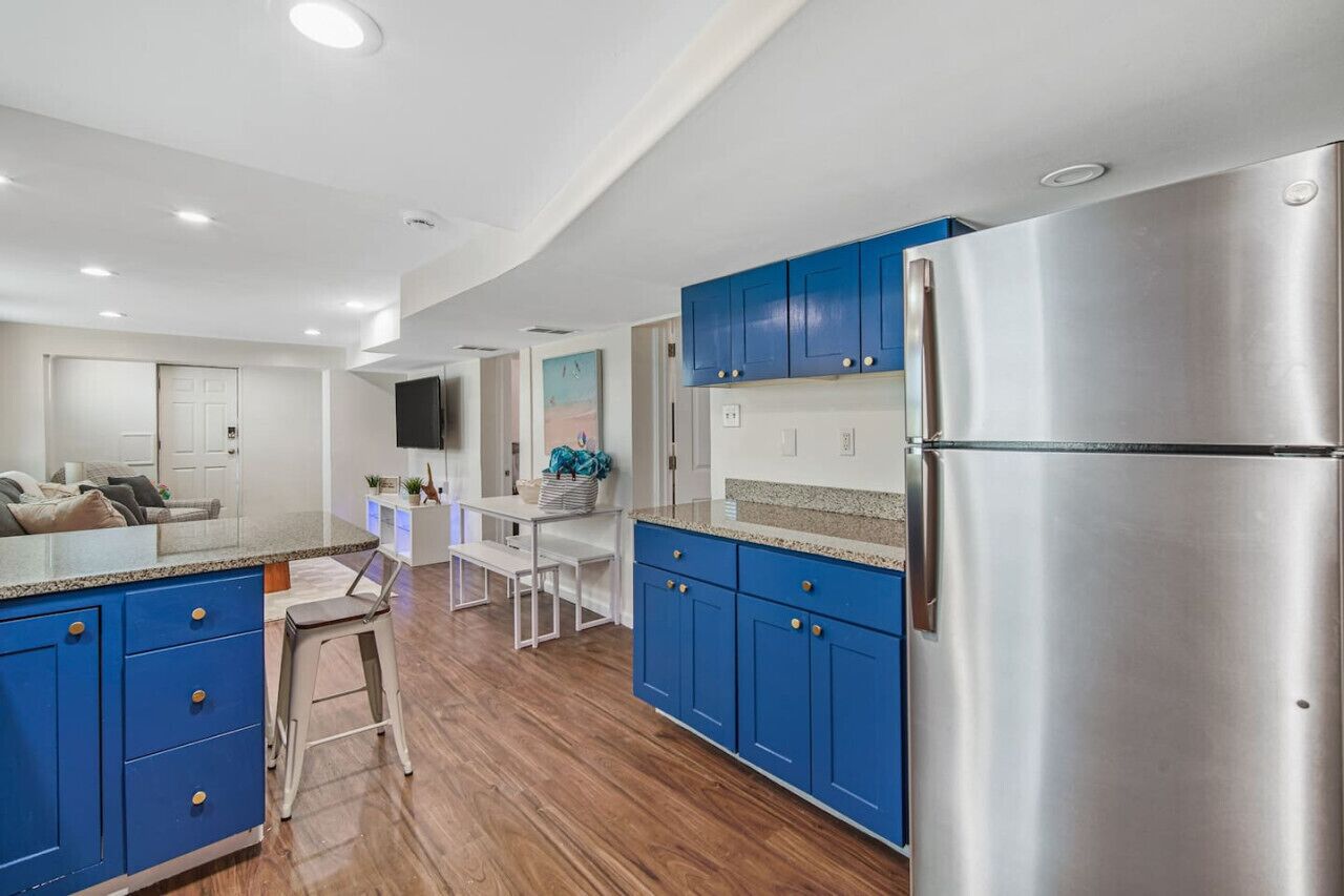 A modern kitchen with blue cabinets, a stainless steel refrigerator, and a dining area with a white table and bench.