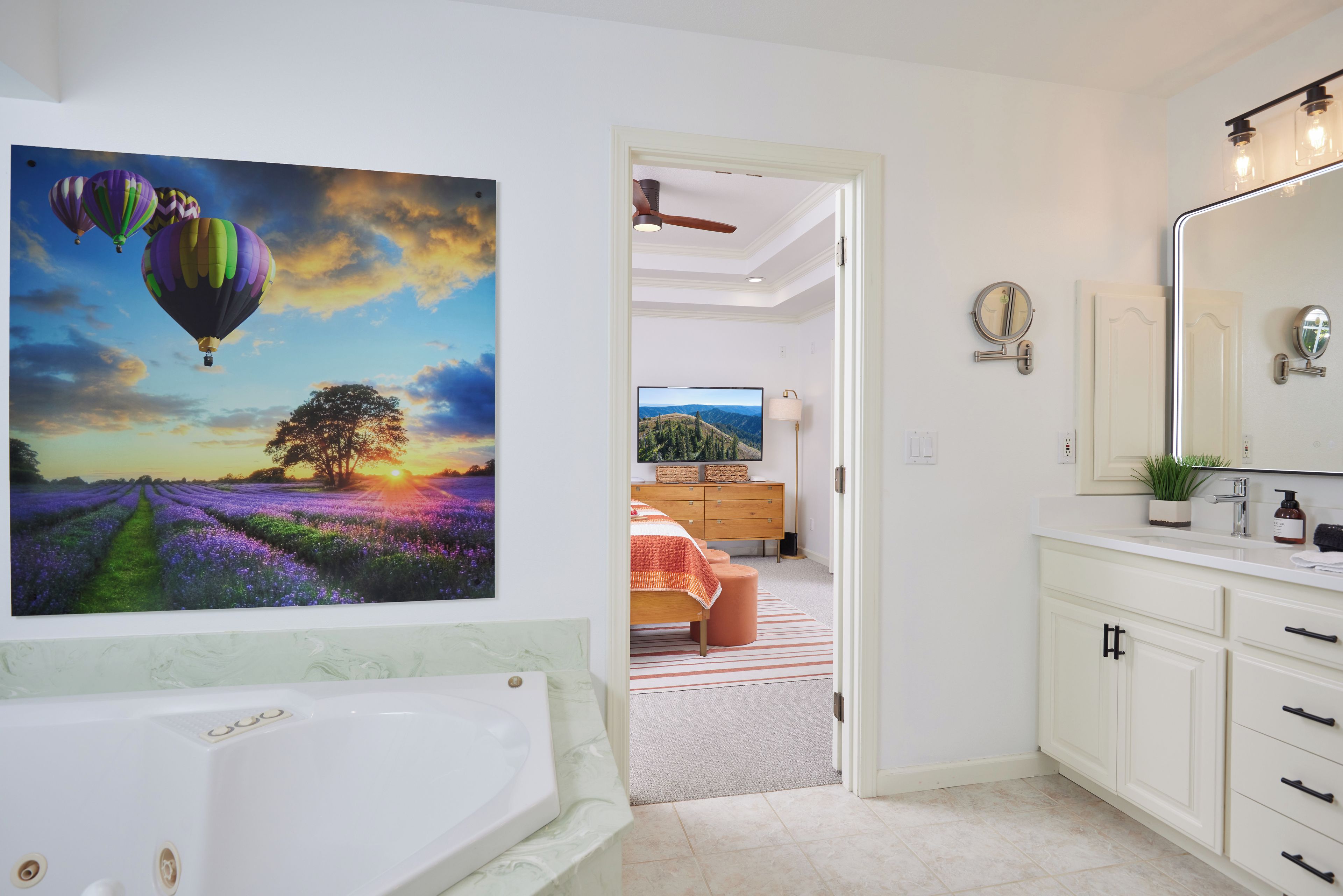 Une salle de bain avec un grand miroir, une baignoire et un tableau représentant des montgolfières.