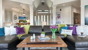 A spacious living room with a high ceiling, a central fireplace, and a view of the dining area.