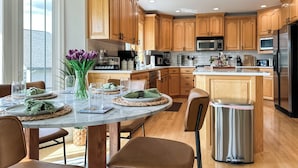 A modern kitchen with wooden cabinets, a stainless steel refrigerator, and a dining area with a marble table and chairs.