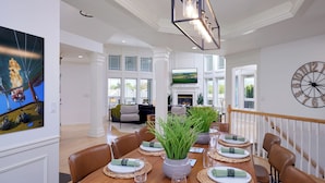 A dining area with a long table set for six, a fireplace, and a large clock on the wall.