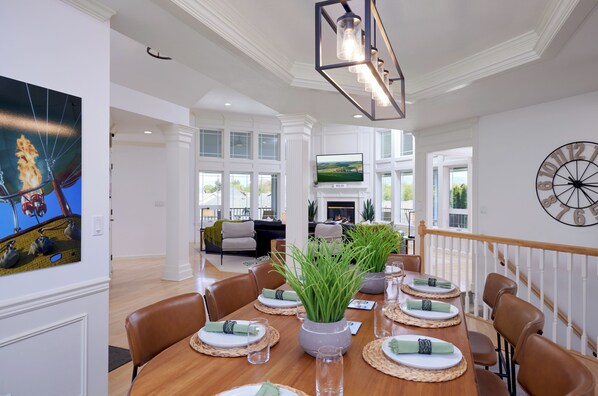 A dining area with a long table set for six, a fireplace, and a large clock on the wall. - Walla Walla 5BR · Fireplace & Arcade · Sleeps 12 (College Place)