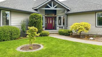 Una casa residencial con un jardín delantero, una puerta roja y un árbol pequeño en el centro.