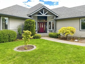 Une maison d’habitation avec un jardin devant, une porte rouge et un petit arbre au centre.