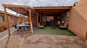A covered outdoor patio with a table and chairs, a green artificial turf area, and a stone floor. - Hostal Pablito (San Pedro de Atacama)