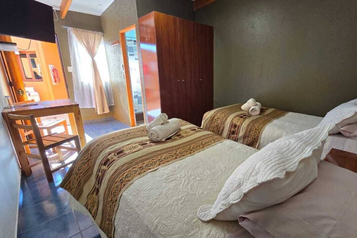 Quarto com duas camas, um guarda-roupa de madeira, uma escrivaninha e uma cadeira.
