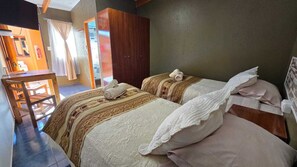 A bedroom with two beds, a wooden wardrobe, a desk, and a chair. - Hostal Pablito (San Pedro de Atacama)