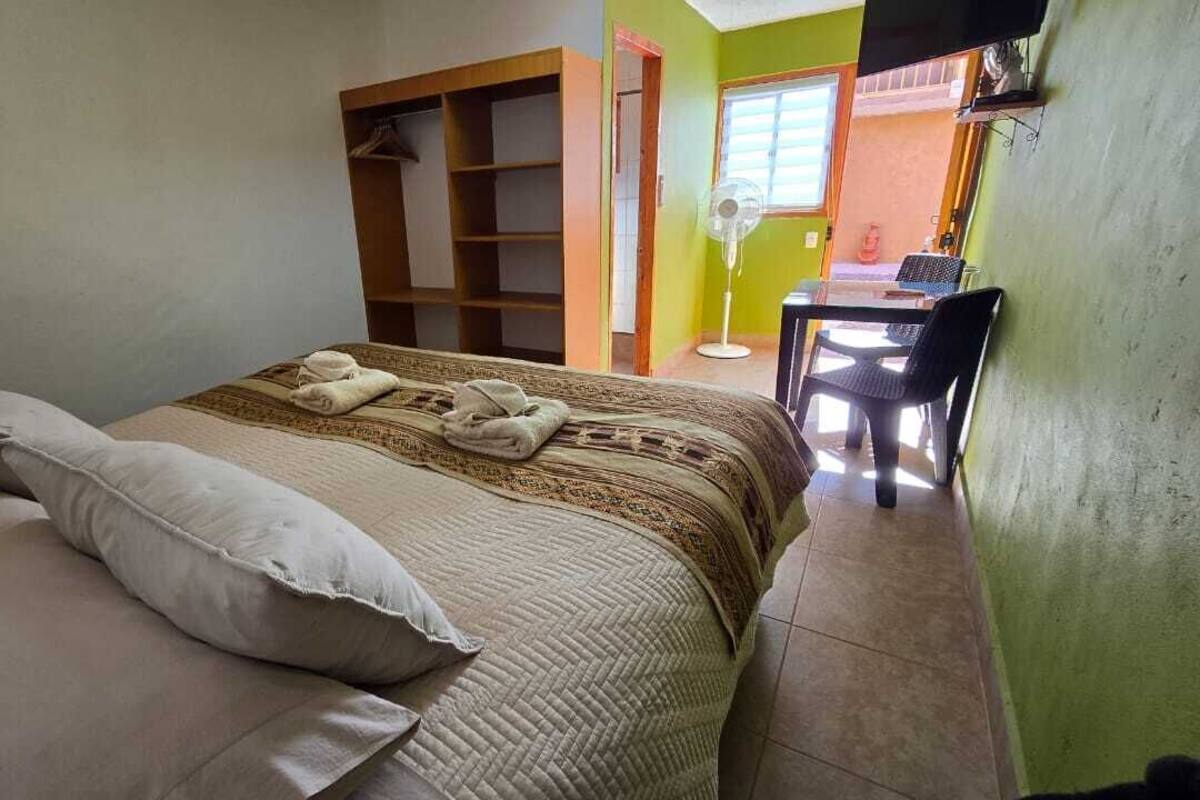 Um quarto com uma cama, um guarda-roupa, uma mesinha com cadeiras e uma televisão.