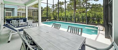 A covered outdoor area with a pool, seating, and a view of trees.