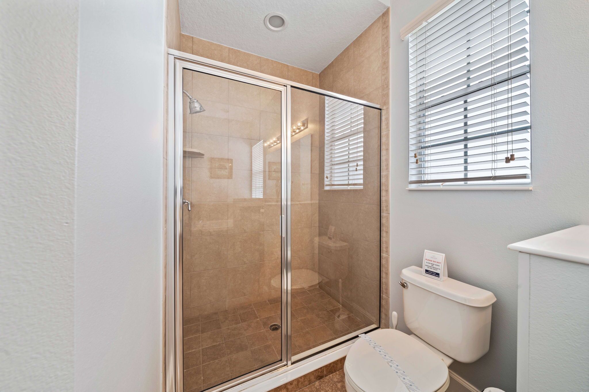 Une salle de bain moderne avec une douche à parois de verre, des toilettes et une fenêtre équipée de stores.