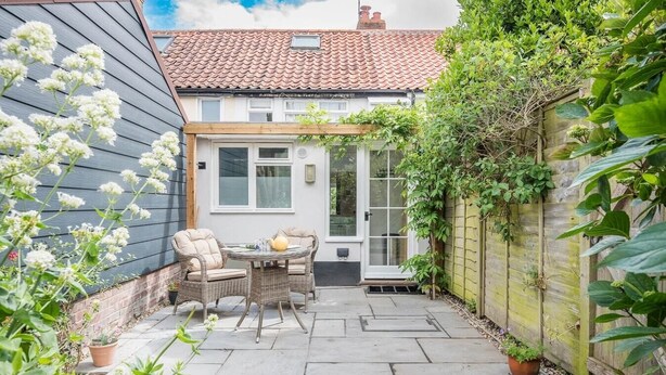A patio with wicker furniture and a table, surrounded by potted plants and a wooden fence. - Angel Cottage, Wenhaston. Nr Southwold and Minsmere (Suffolk)