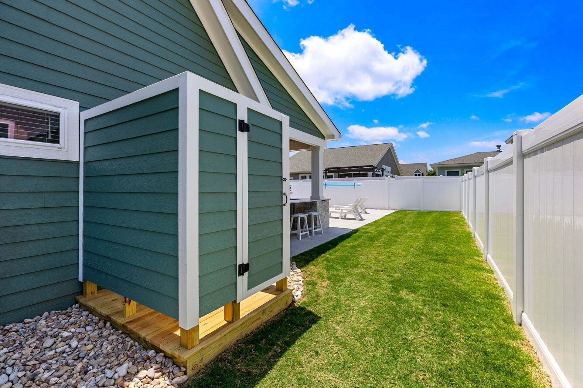 Un jardin avec une terrasse en bois, une clôture blanche et une pelouse bien entretenue.