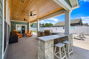 An outdoor patio with a stone bar, wooden chairs, and a ceiling fan.