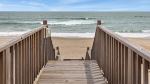 Une promenade en bois menant à une plage, avec des vagues en arrière-plan.