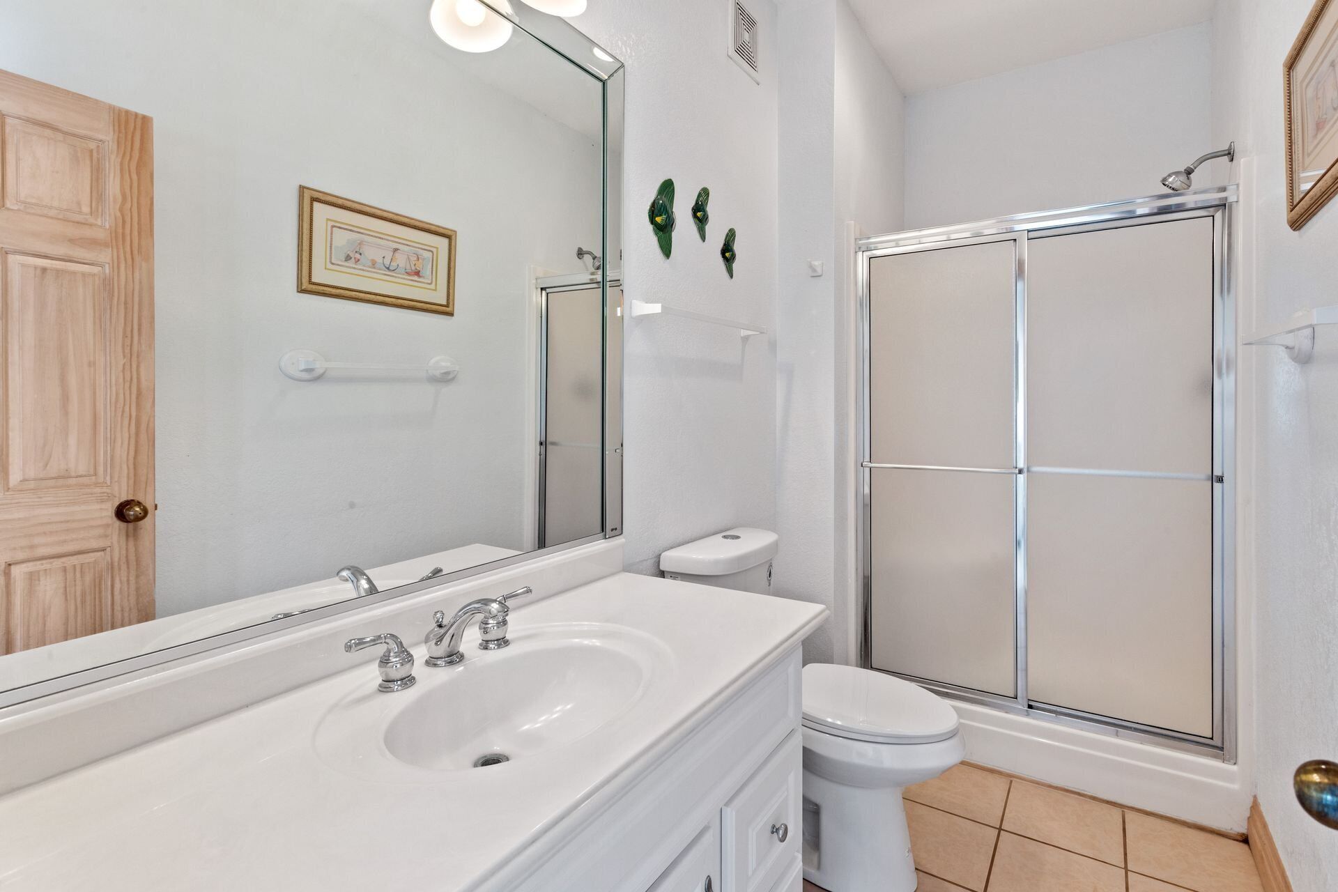 Un baño con lavamanos blanco, espejo, inodoro y cabina de ducha de vidrio.