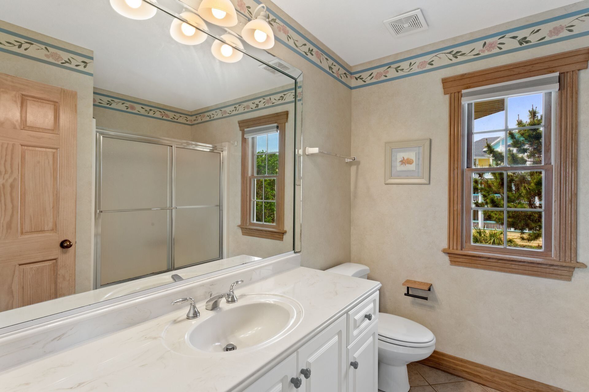 A bathroom with a large mirror, a sink, a toilet, and a window with a view of greenery.