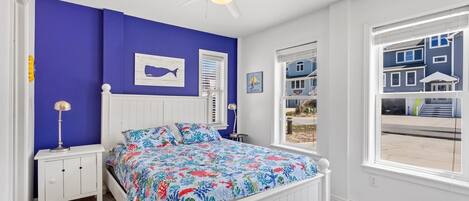 A bedroom with a bed, a nightstand, a ceiling fan, a window with a view of buildings, and a wall with a whale painting.