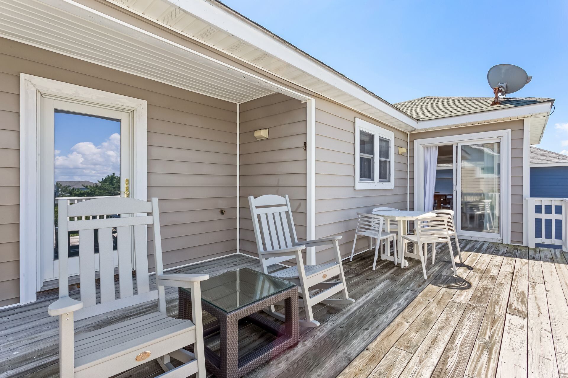A covered outdoor deck with white furniture, including chairs and a table, and a glass-top table.