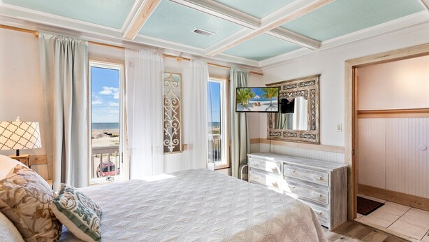 Une chambre avec un grand lit, une commode, une télévision et une vue sur la plage.