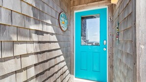 Une porte turquoise avec une petite fenêtre, un mur recouvert de bardeaux de bois et une enseigne avec un logo et du texte.