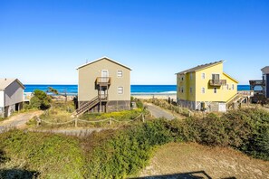 A coastal property with a wooden staircase leading to a house, a beach in the background, and a clear sky.