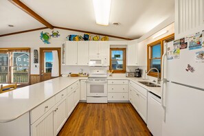 Une cuisine avec des meubles blancs, un plancher en bois, un four à micro-ondes, une cuisinière et un réfrigérateur.