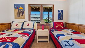 Une chambre avec deux lits, chacun recouvert d’une courtepointe à motifs marins. Une fenêtre offre une vue sur un bâtiment situé à l’extérieur.