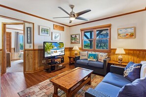 A living room with a television, wooden furniture, and a window with a view of a house.