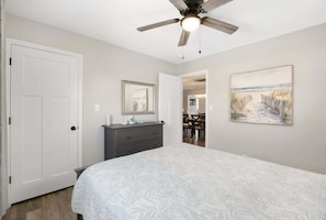 Une chambre à coucher avec un lit, une commode, un ventilateur de plafond et un tableau accroché au mur.