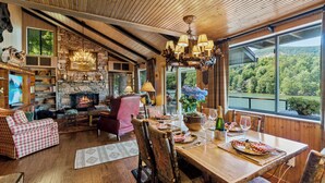 A cozy living room with a stone fireplace, wooden ceiling, and large windows offering a scenic view.