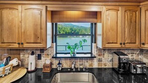 A kitchen with wooden cabinets, a sink, a window with a view of a lake, and a toaster.