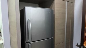 Cocina compacta con refrigerador de acero inoxidable, armarios de madera y piso de baldosas.