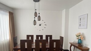 Un comedor con una mesa y sillas de madera, una lámpara colgante y una mesita con un jarrón de flores.