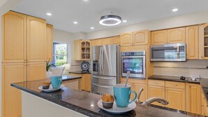 A modern kitchen with wooden cabinets, stainless steel appliances, and a granite countertop. - Canalside 4BR villa with pool, spa, dock, and Gulf access. (Cape Coral)