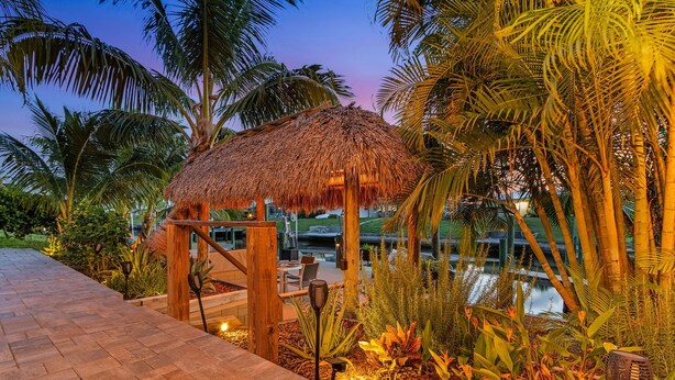 A thatched-roof structure surrounded by palm trees and a pool. - Canalside 4BR villa with pool, spa, dock, and Gulf access. (Cape Coral)