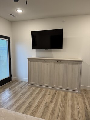 A room with a flat-screen TV mounted on the wall, a wooden cabinet below it, and a door with blinds. - Amazing Table Rock Views with Private Hot Tub, Theatre Room & Free Daily Branson Attraction Tickets (Hollister)