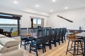 A modern dining area with a large table and chairs, a balcony with a view of the landscape, and a ceiling fan. - Amazing Table Rock Views with Private Hot Tub, Theatre Room & Free Daily Branson Attraction Tickets (Hollister)