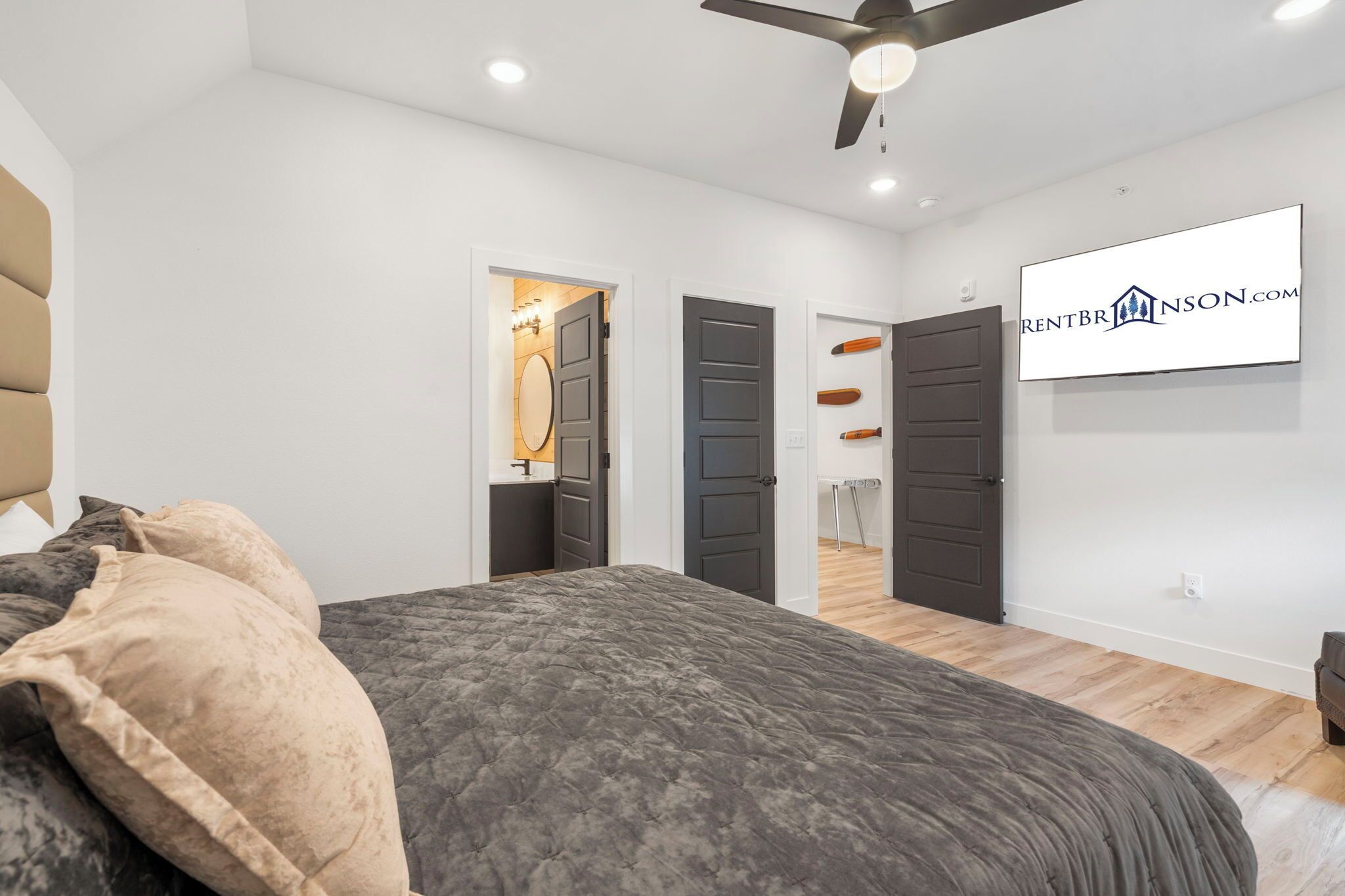 A modern bedroom with a bed, a ceiling fan, and a TV mounted on the wall.