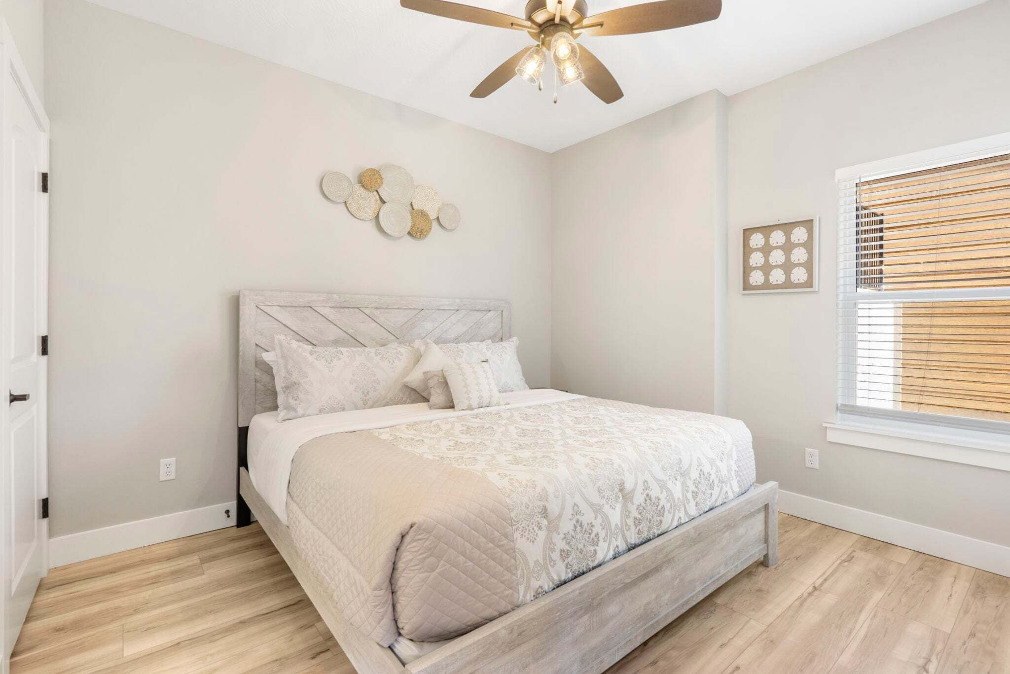 A bedroom with a bed, a ceiling fan, a window with blinds, and a wall clock.