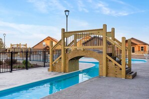 A wooden bridge over a swimming pool with a metal fence and houses in the background.