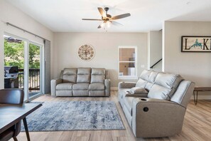 A modern living room with a sofa, a recliner, a coffee table, a rug, a ceiling fan, and a clock on the wall.