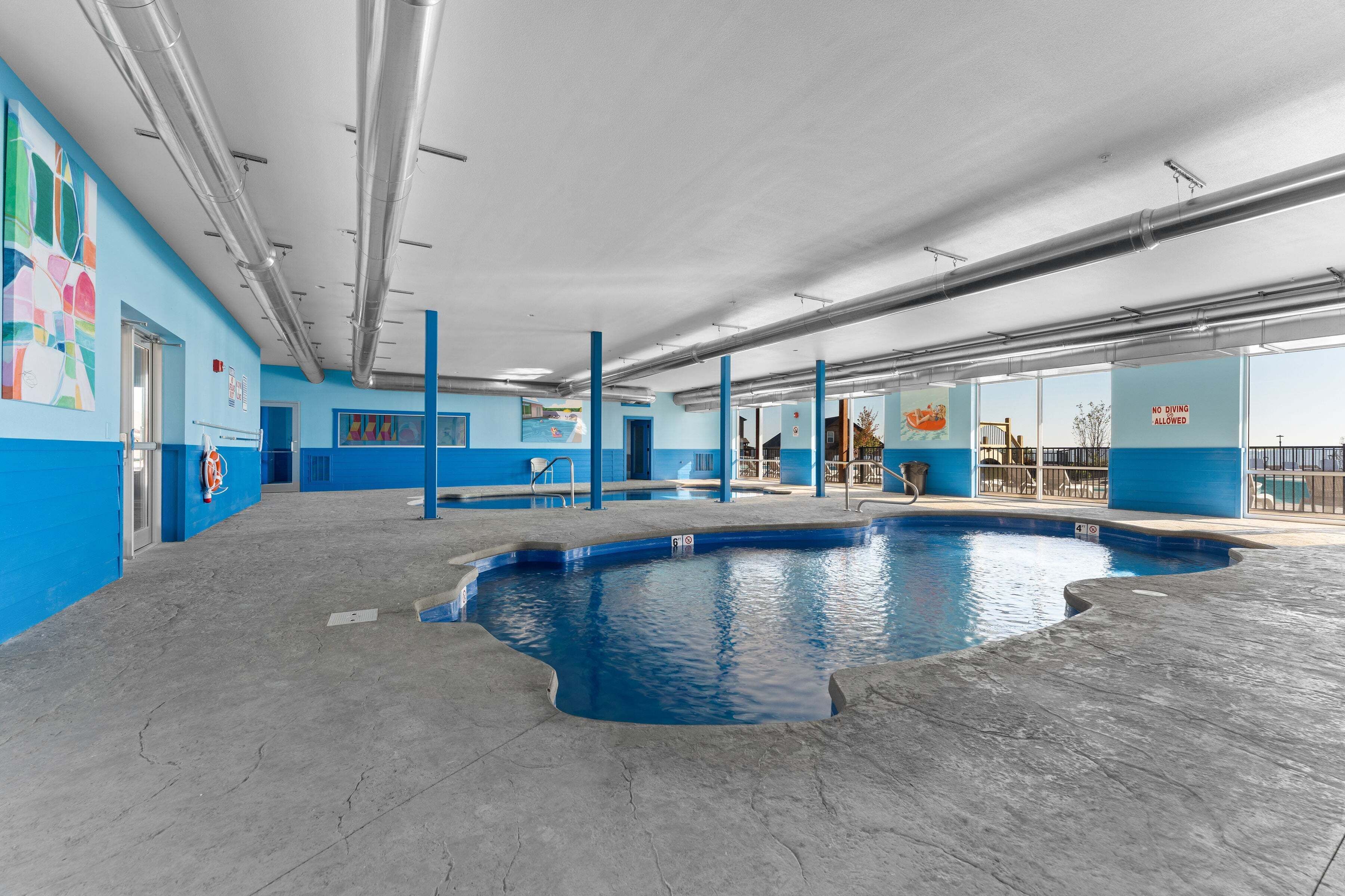 A swimming pool area with blue walls, a clear ceiling, and visible pipes.