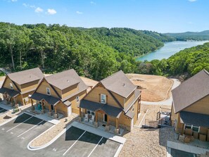 A multi-story lodge with a parking lot and a view of a lake surrounded by forest.