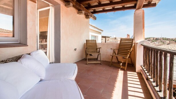 Un balcone con un divano, due sedie di legno e vista sulla città.