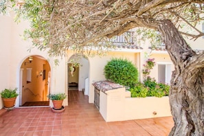 A courtyard with a tiled floor, potted plants, a tree, and a building with an arched entrance. - Splendid 93 sqm apartment on two levels, ideal for 6 people, located on the ground floor of a building WITHOUT a lift (stairs to access it). The accommodation is located in an exclusive area in Porto Cervo, a few steps from the center and the characteris (Porto Cervo)