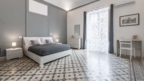 Un dormitorio con cama, mesitas de noche, un escritorio y un amplio ventanal con cortinas.