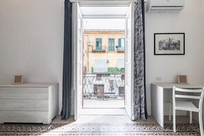 Une pièce avec vue sur un balcon, un bureau blanc, une chaise, un sol à motifs et un tableau encadré au mur.